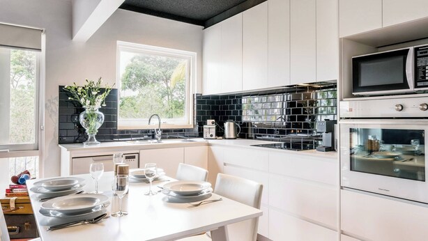 Une cuisine moderne avec des meubles blancs, un pare-feu noir et des appareils électroménagers en acier inoxydable.