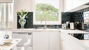Une cuisine moderne avec des meubles blancs, un dosseret de carreaux noirs, une fenêtre donnant sur les arbres, un évier en acier inoxydable et un grille-pain.