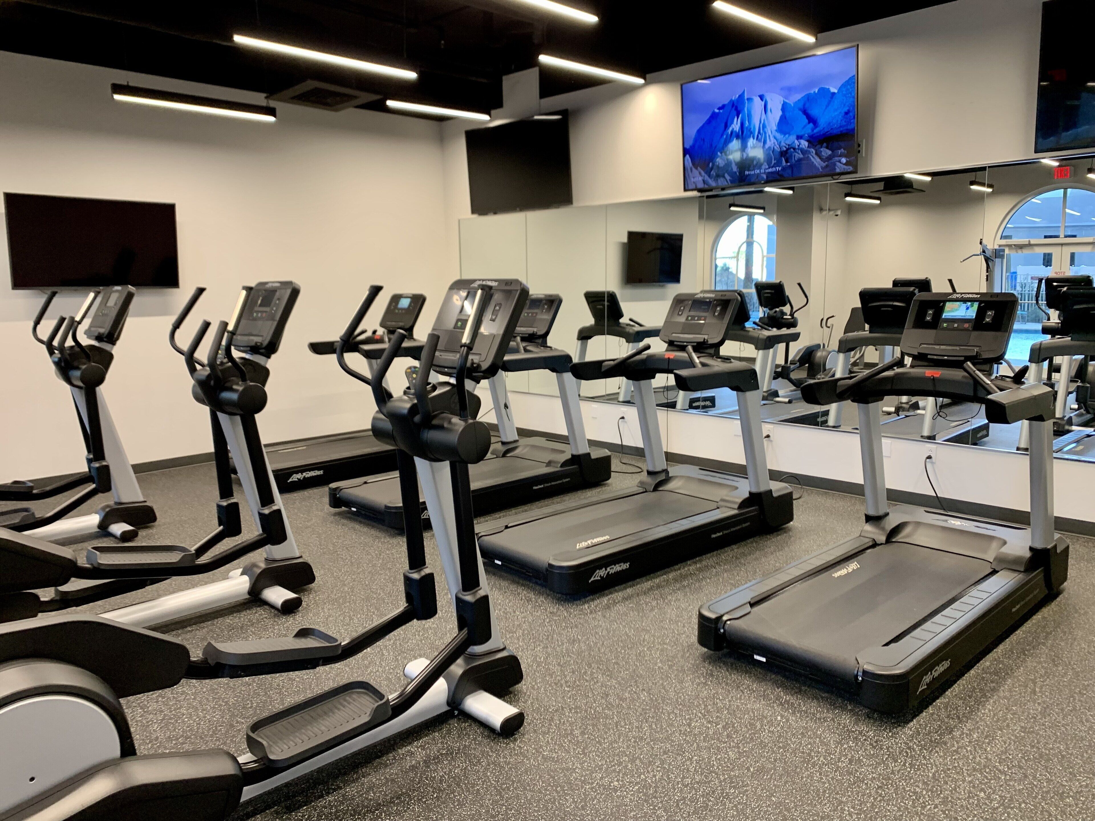 Ein Fitnessstudio mit mehreren Laufbändern und Ergometer, einem großen Bildschirm und einem modernen Design.