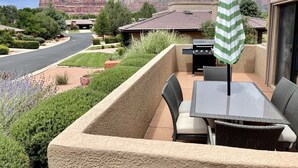 Una veranda con barbecue, tavolo e sedie da esterno, immersa in un giardino curato e con vista sulle montagne.