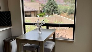 Zona pranzo con tavolo e due sedie, una finestra con vista su formazioni rocciose rosse e un cestino.