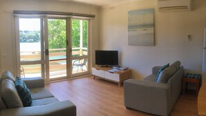 Uma sala de estar com dois sofás, uma televisão e uma porta de vidro deslizante para uma varanda.