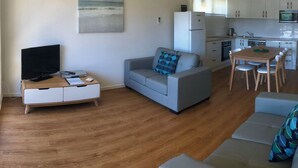 Uma sala de estar moderna com um sofá cinzento, uma TV sobre um suporte de madeira e uma pintura de uma praia.