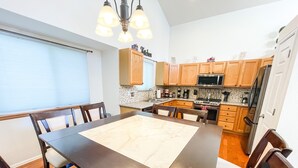 A modern kitchen with wooden cabinets, a stainless steel refrigerator, and a dining area with a large table and chairs. - 2 Master Suites/3 King Beds/4 Bath/Mins to Airport (Colorado Springs)
