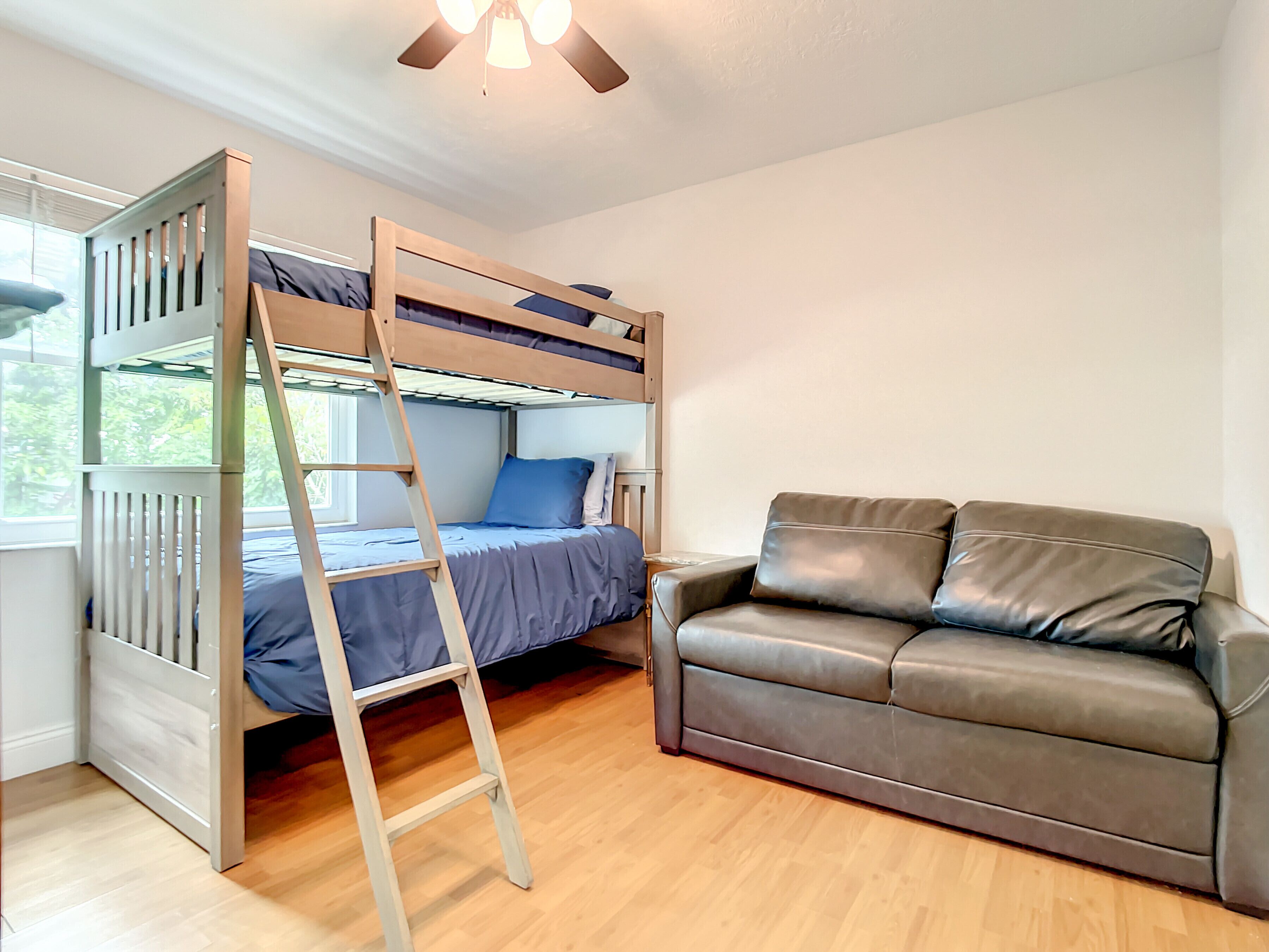 A bunk bed with a ladder, a brown leather sofa, and a ceiling fan.