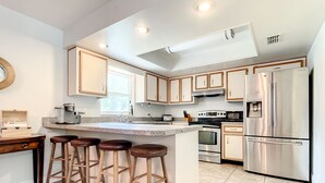 A modern kitchen with a central island, bar stools, stainless steel appliances, and a window providing natural light. - 💎Red Rooster cottage🌅💎🏄🏽‍♂️ (Port Orange)