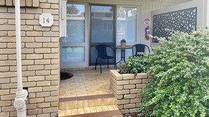 Une maison en briques avec le numéro « 14 » peint sur le mur, une véranda couverte avec une table et des chaises, et un extincteur fixé au mur.