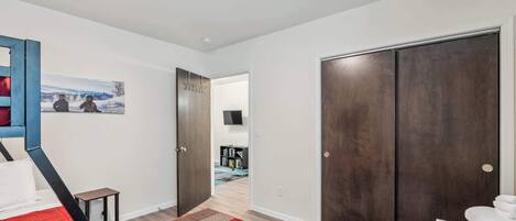 A bedroom with a bed, a red and beige checkered rug, a dark wooden wardrobe, and a hallway leading to a bathroom.
