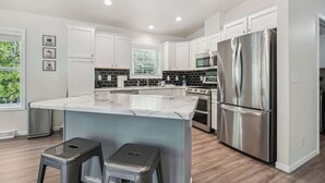 A modern kitchen with white cabinets, stainless steel appliances, a marble island, and two stools. - Livin' the Dream in Fish Creek! (Fish Creek)