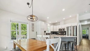 A modern kitchen with white cabinets, stainless steel appliances, and a wooden dining table. - Livin' the Dream in Fish Creek! (Fish Creek)