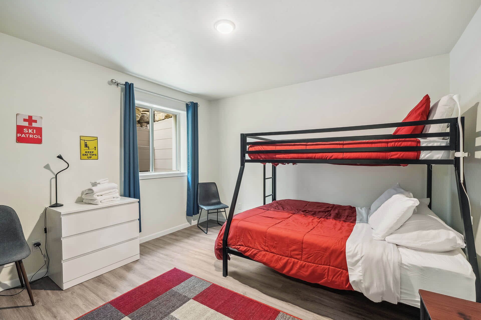 A bunk bed room with a desk, chair, and a window with curtains.