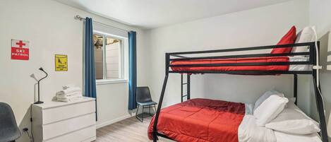 A bunk bed room with a desk, chair, and a window with curtains.