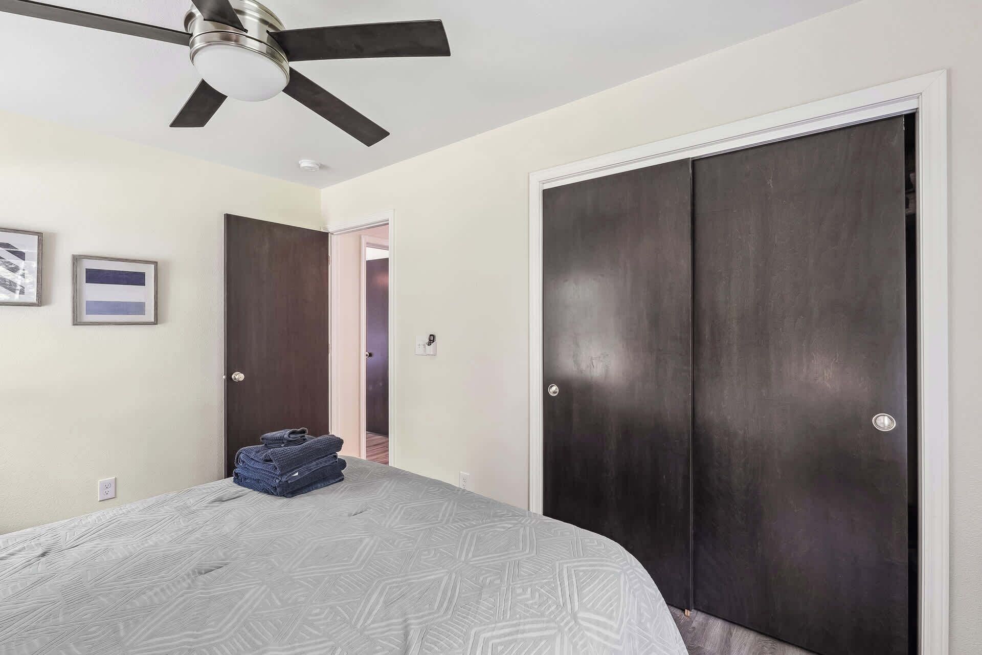 A bedroom with a bed, a ceiling fan, a dark wooden wardrobe, and a door leading to another room.