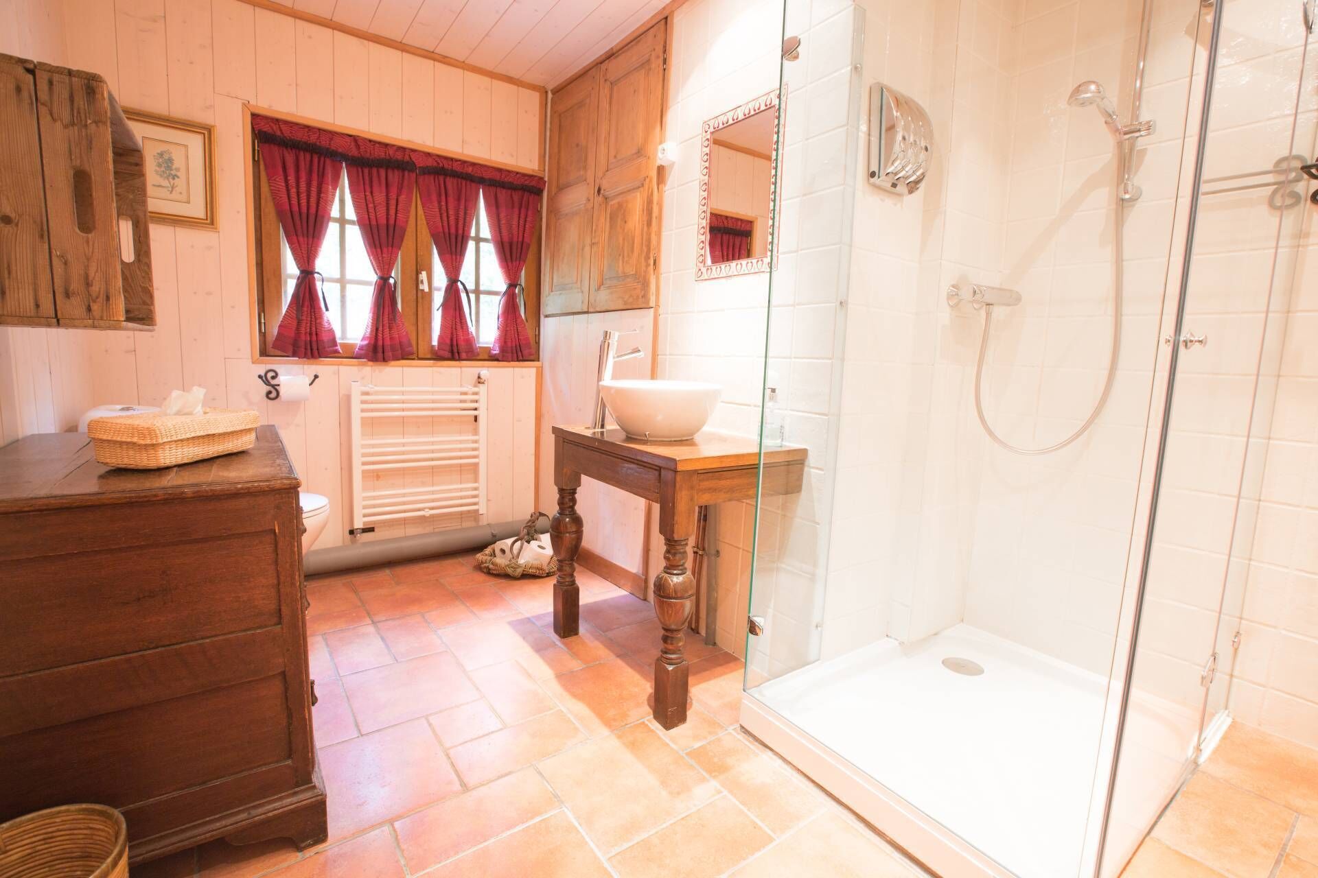 Une salle de bain avec une commode en bois, un lavabo avec un receveur, une cabine de douche en verre et un radiateur.
