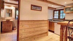 A rustic kitchen with wooden cabinetry, a large island, and a window overlooking greenery. - Savoyard Farmhouse - Sleeps 14, Garden & Parking (Araches-la-Frasse)