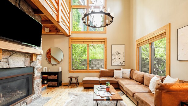 A cozy living room with a fireplace, wooden beams, a sofa, a coffee table, and large windows. - Year-Round Fun - Central Location, Private Hot Tub & 5-Min Walk to Free Shuttle! (Park City)