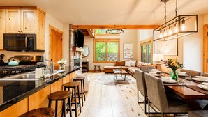 A kitchen with wooden cabinets, a microwave, and a stove. There is a dining area with a table set for two, a sofa, and a TV mounted on the wall. - Year-Round Fun - Central Location, Private Hot Tub & 5-Min Walk to Free Shuttle! (Park City)
