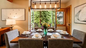 A dining area with a table set for four, a vase with flowers, and a view of greenery through a window. - Year-Round Fun - Central Location, Private Hot Tub & 5-Min Walk to Free Shuttle! (Park City)