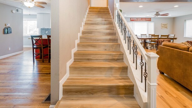 Eine Treppe mit Holzboden und weißen Geländern, die zu einem Essbereich mit einem roten Tisch und Stühlen führt.