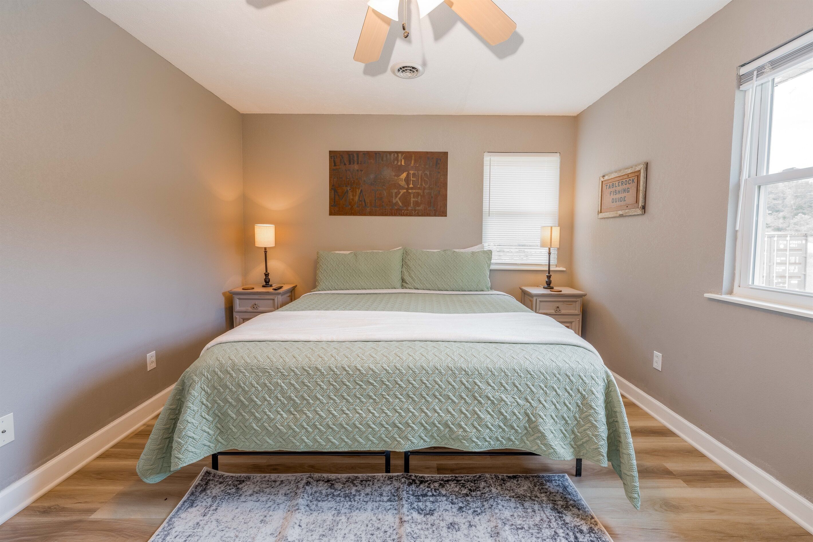 A bedroom with a bed, nightstands, a wall clock, a window, and a painting.