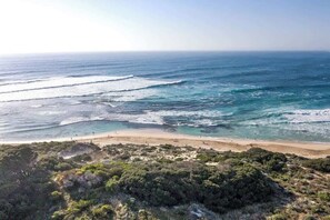 A coastal landscape with a beach, ocean waves, and dense vegetation.