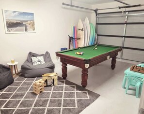 A room with a pool table, bean bag chairs, a small table with a drink, and a garage door.