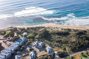 Ett flygbildsfoto av en fastighet vid kusten med en strand, en parkeringsplats och en rad hus med blå tak.
