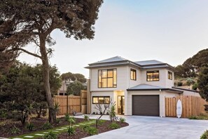 A modern two-story house with a garage, surrounded by a landscaped garden and a wooden fence.