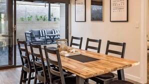 Un comedor con una mesa de madera, sillas negras y un ventanal que da a una zona de estar al aire libre.