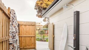 Una reja de madera que da a un espacio exterior cubierto, con una tabla de surf apoyada contra una pared.