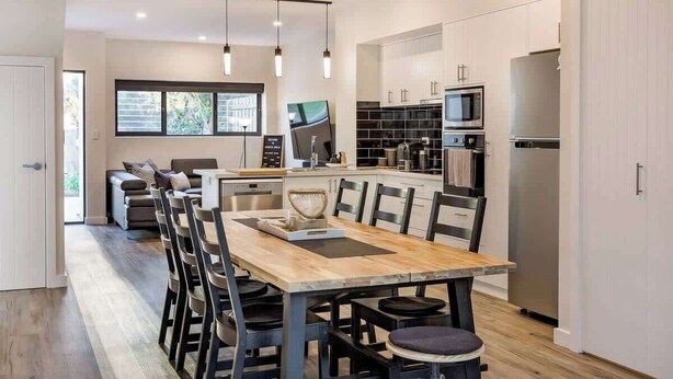 Una cocina moderna con una isla central, electrodomésticos integrados y un comedor con mesa y sillas de madera.