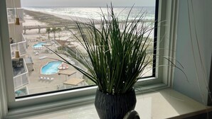 Vista desde la ventana a una piscina y una playa, con una planta en maceta en el alféizar.