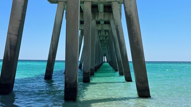 Un muelle que se adentra en aguas turquesas cristalinas, con una playa arenosa al final.