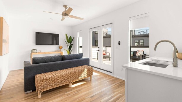 Un salon moderne avec un canapé, un banc, un téléviseur et un ventilateur de plafond.