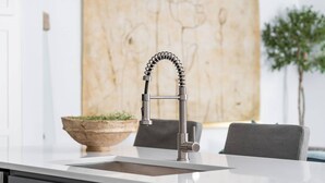 Une cuisine moderne dotée d’un robinet en acier inoxydable, d’un plan de travail blanc et d’un saladier en bois contenant des plantes vertes.