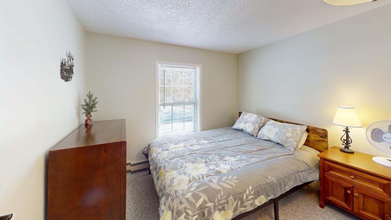 A bedroom with a bed, a nightstand, a dresser, a window, and a wall decoration.