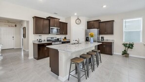 Une cuisine moderne avec des meubles de rangement en bois foncé, un îlot central doté de tabourets, un four à micro-ondes et un réfrigérateur.