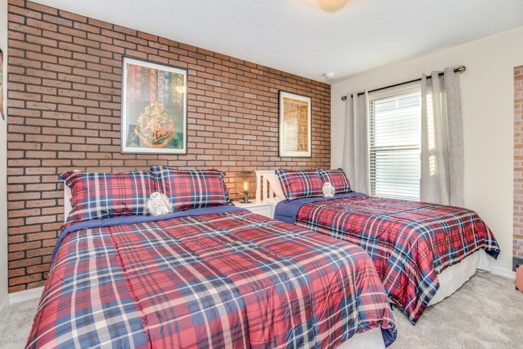 A room with two beds, each with a red and blue plaid bedspread, a brick wall, and two framed pictures.