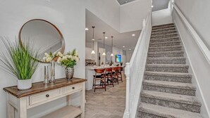 A staircase leading to a dining area with a wooden console table and a mirror. - Luxury Home 7 Bedrooms Near Disney! 7 Villa by RedAwning (Kissimmee)