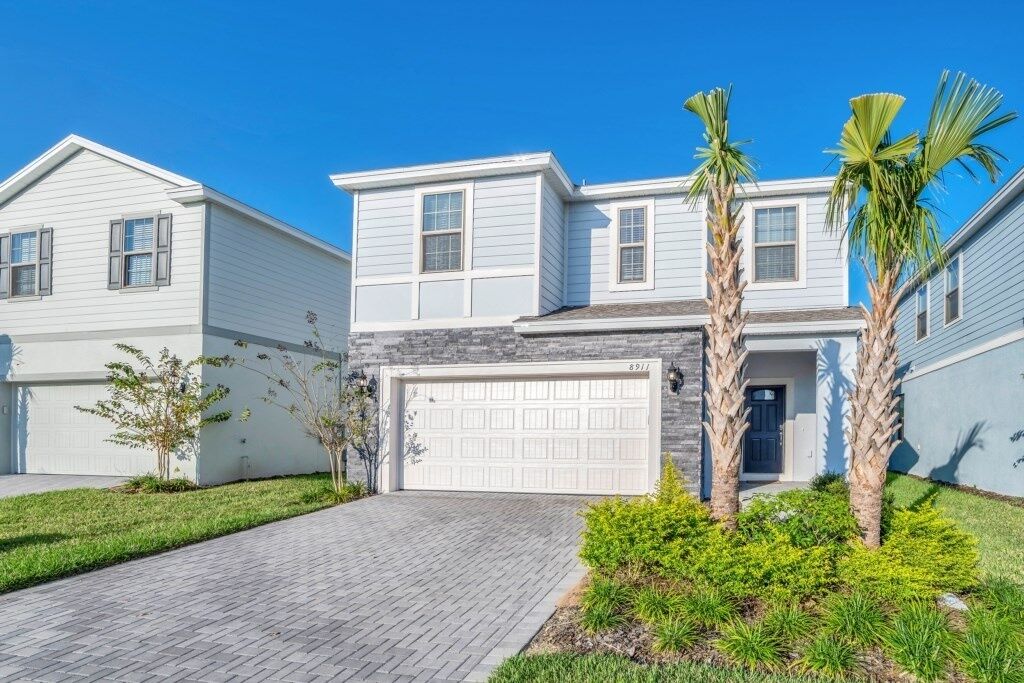 A two-story house with a garage, a paved driveway, and palm trees.