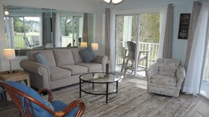 A spacious living room with a large sofa, a round coffee table, and a wicker chair. There is a balcony with outdoor seating. - 406m 1 Bedroom Condo by RedAwning (Calabash)