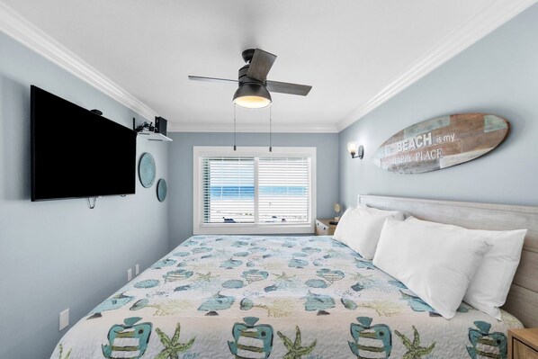 A bedroom with a bed, a ceiling fan, a TV, a window with blinds, and a decorative wall piece.