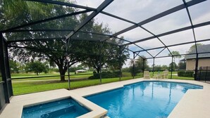 Une piscine extérieure dotée d’un espace couvert, entourée d’arbres et d’une pelouse.