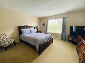 A bedroom with a bed, a chair, a dresser, a television, and a window with curtains. - Golf Views By The Pool! Southern Dunes Golf Home 5 Bedroom Villa by RedAwning (Haines City)