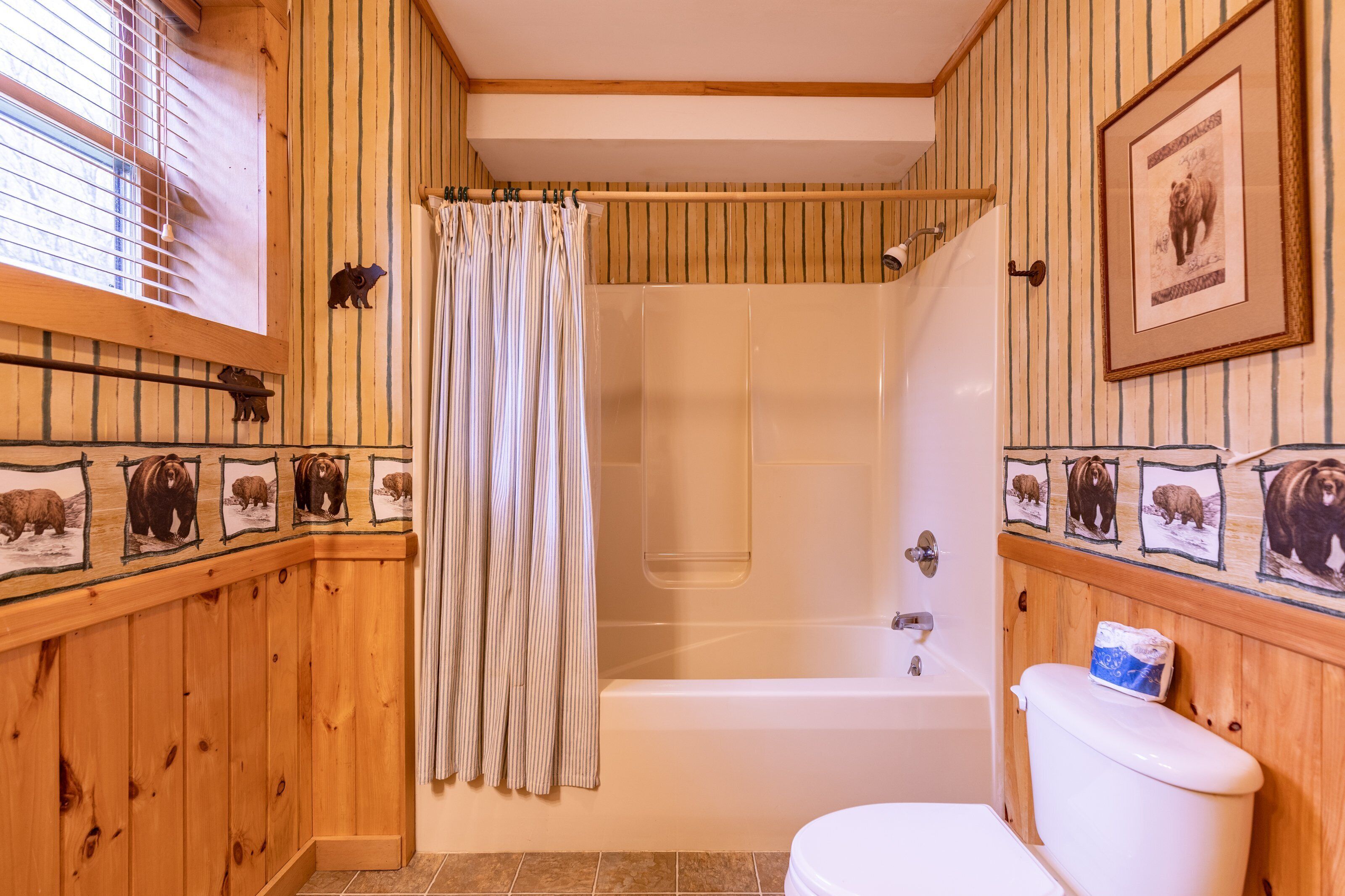 A wooden-paneled bathroom with a bathtub, toilet, and shower curtain.