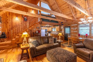 A rustic cabin interior with a wooden staircase, a dining area, and a living room with a sofa and ottoman. - Welcome to The Nut House- hot tub, pet friendly, fireplace (Seven Devils)
