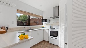 A modern kitchen with white cabinets, a stainless steel sink, a stove, and a microwave. - Valley Palms - Mt Maunganui Holiday Home (Mt Maunganui)