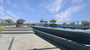 Un espace piscine aménagé sur le toit, offrant une vue dégagée sur le paysage environnant, un coin salon doté d’un grand parasol et une piscine bordée de carreaux bleus.