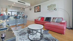 Un salon moderne avec un canapé rouge, une table basse ronde et un coin cuisine à l’arrière-plan.