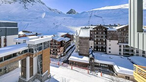 A snow-covered mountain town with modern buildings, including a hotel with balconies and a ski lift visible in the background. - Les Genepis (Val Claret) by Interhome (Tignes)